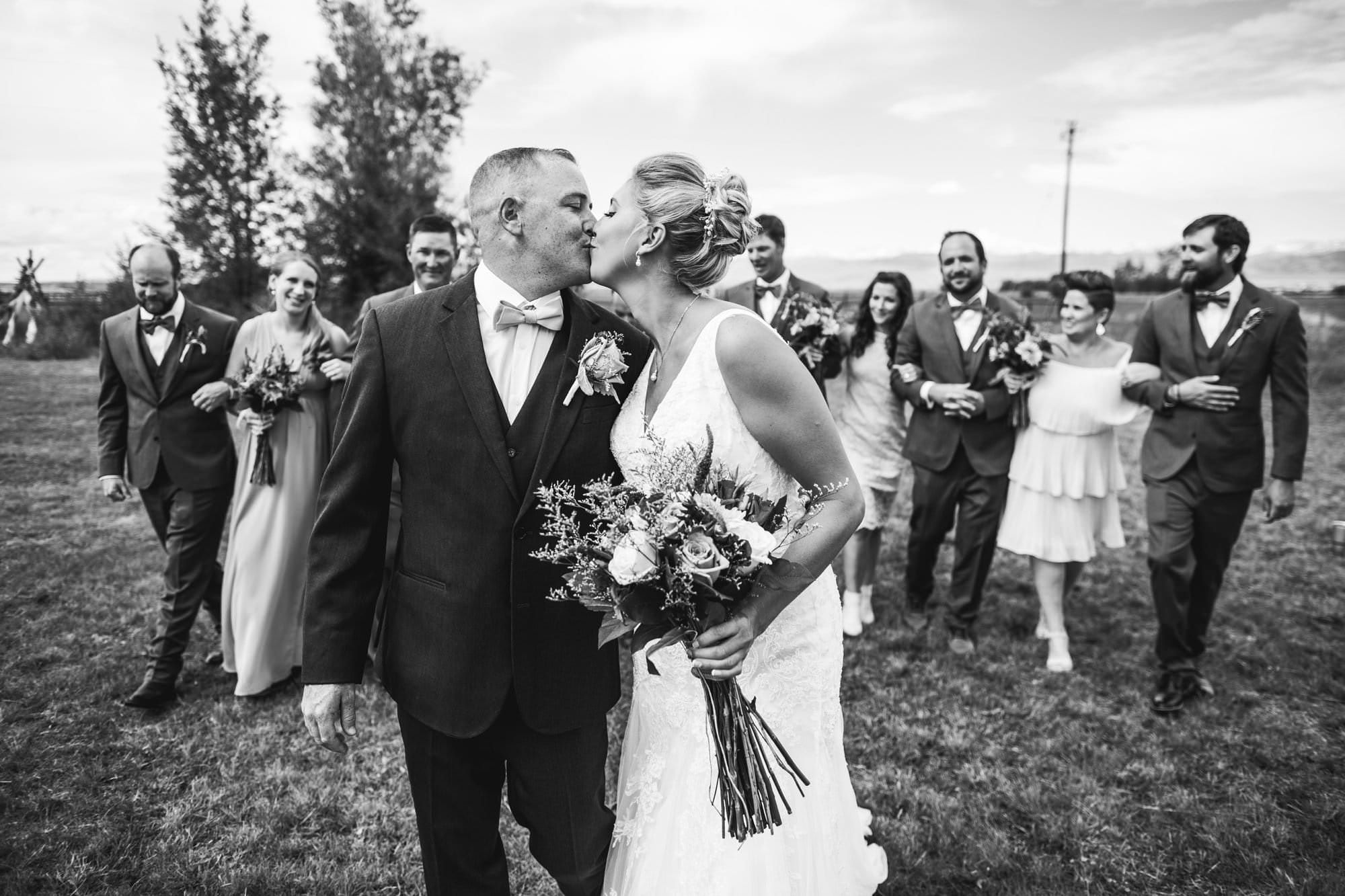 bride and groom kissing with wedding party behind